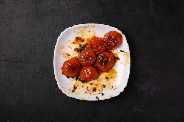 어두운 배경, 복사 공간에 기름의 흔적과 함께 하얀 접시에 구운 민트 체리 토마토