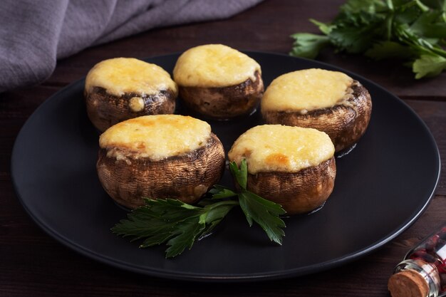 Funghi al forno ripieni di formaggio ed erbe su un piatto nero. fondo in legno.