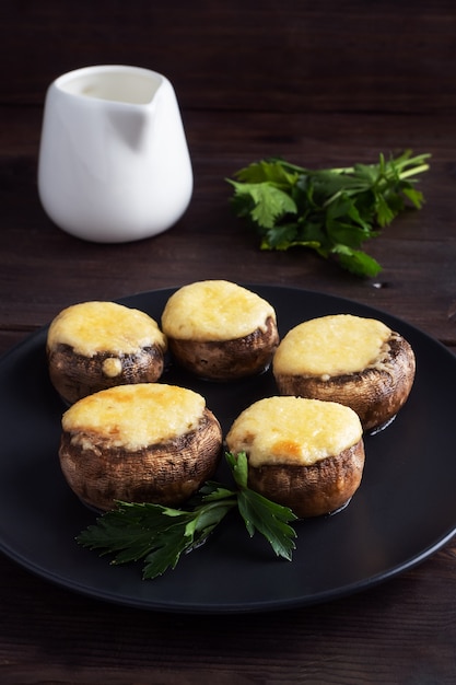 Baked mushrooms stuffed with cheese and herbs on a black plate. wooden table.