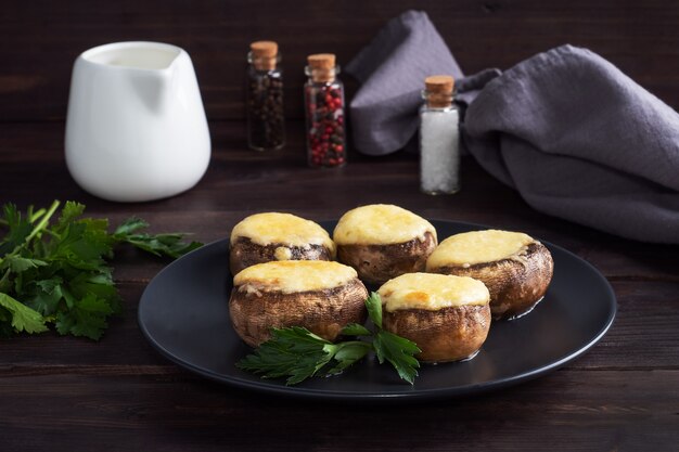 Baked mushrooms stuffed with cheese and herbs on a black plate. wooden table.