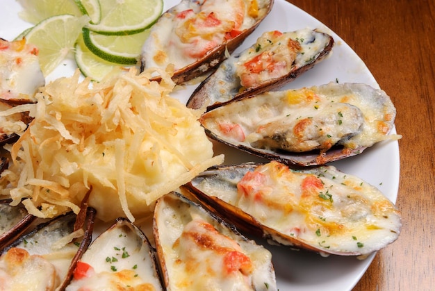 Baked mussels au gratin with mashed potatoes on a white plate on wooden table Brazilian seafood