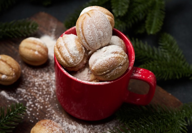 Baked nut-shaped dessert in a red ceramic mug sprinkled with powdered sugar, top view