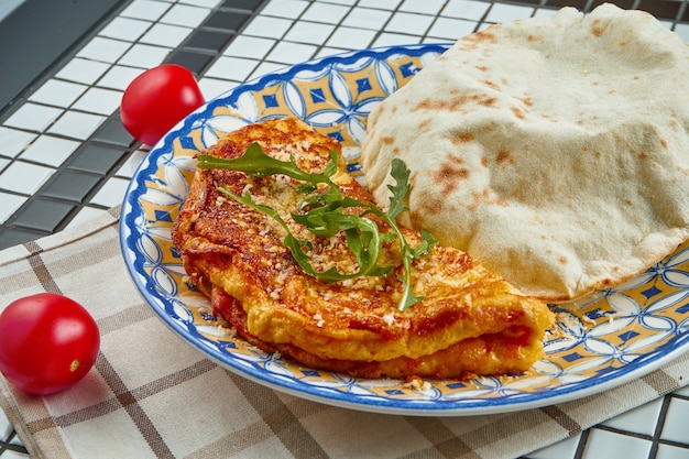 Baked omelet with parmesan and arugula with focaccio bun on an unusual ceramic plate in a composition with ingredients Close up view.