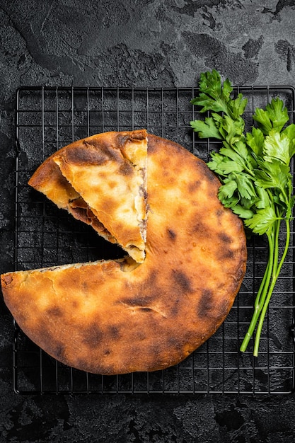 Baked Ossetian pie with beef meat and herbs Black background Top view