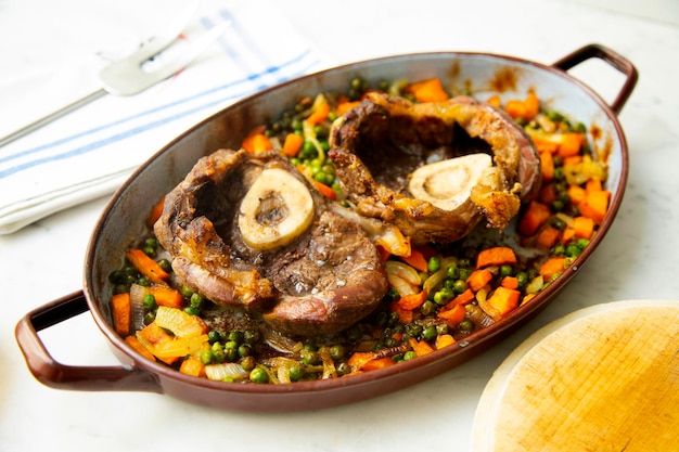 Baked Ossobuco cooked at low temperature on a bed of vegetables and potatoes