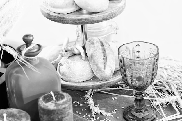 Baked pasty or bread on wooden tray near glass bocal and candle with spikelet laying on table with nobody on christmas or easter celebration