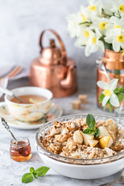 Baked pear crumble with pears and honey in a white dish on the table with copper utensils and flowers