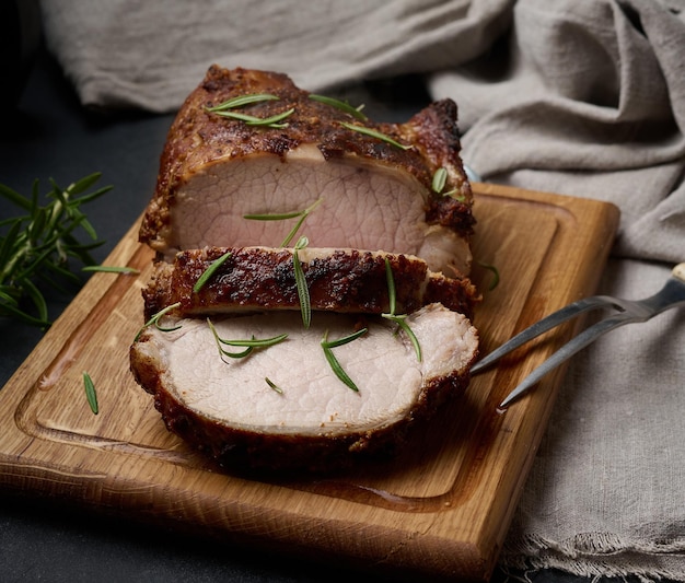 Baked piece of pork meat in spices on a wooden board, cut into pieces. Eye of round roast steak