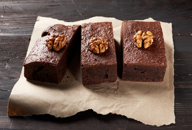 Baked pieces of brownie chocolate cake with nuts on a brown piece of paper, top view, delicious dessert