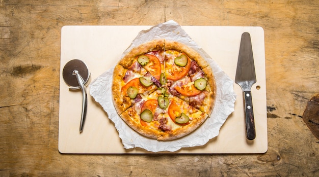 Baked pizza with bacon and tomatoes. On wooden table.