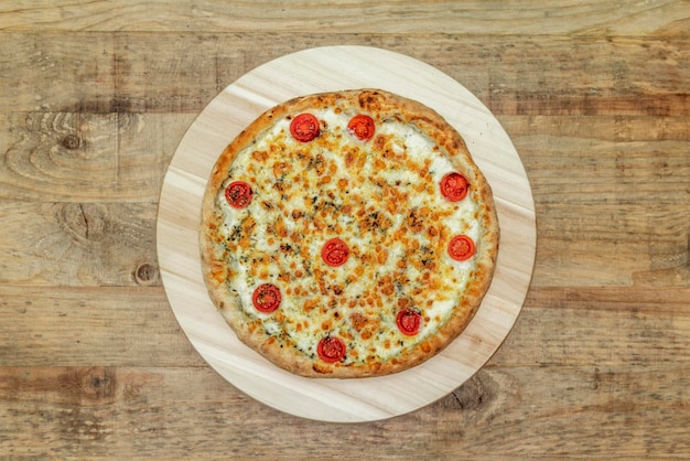 Baked pizza with mozzarella and four cheeses with cherry tomatoes on wooden table