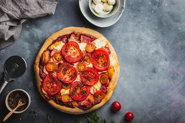 Baked pizza with whole grain dough, tomato, ham, mozzarella, tomato sauce, thyme served on gray stone background with various ingredients for cooking. pizza preparation.