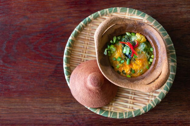 Photo baked poached eggs with cheese spinach scallions in clay pot on a bamboo plate