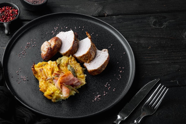 Baked pork fillet loin with potatoe and herbs set, on plate dish, on black wooden table background , with copyspace  and space for text