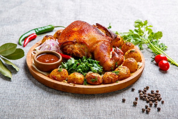 Photo a baked pork leg, overlaid with baked potatoes, lies on a wooden platter.