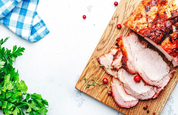 Lonza di maiale al forno intera e pezzi di carne tagliati sul tagliere con spezie erbe e mirtilli rossi vista dall'alto dello sfondo bianco del tavolo da cucina