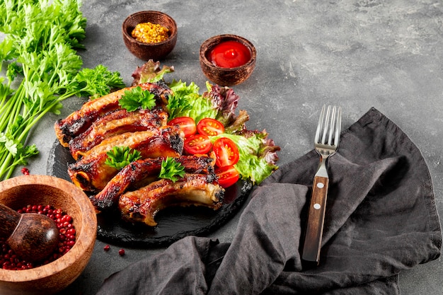 baked pork ribs with vegetables mustard and ketchup on gray background free space for text