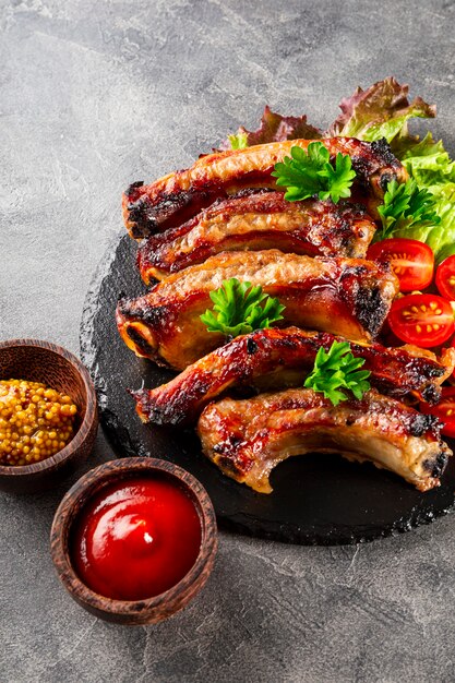 baked pork ribs with vegetables mustard and ketchup on gray background vertical photo