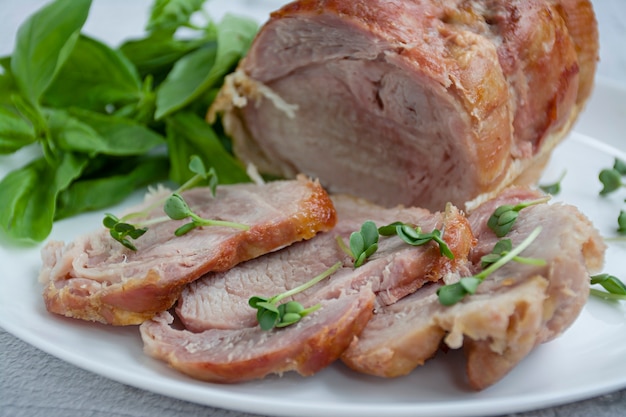 Baked pork roll with greens served on a white plate. 