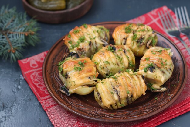 Baked potato-harmonica with mushrooms and cheese located in a plate on dark 