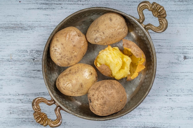 Baked potato in a metal bowl on a wooden table simple vegetarian food Boiled potatoes on wooden table close up