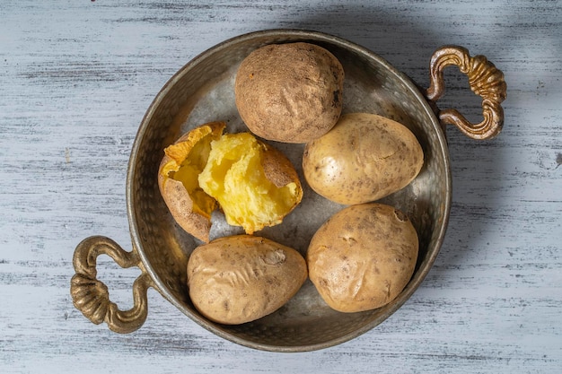 Baked potato in a metal bowl on a wooden table simple vegetarian food Boiled potatoes on wooden table close up