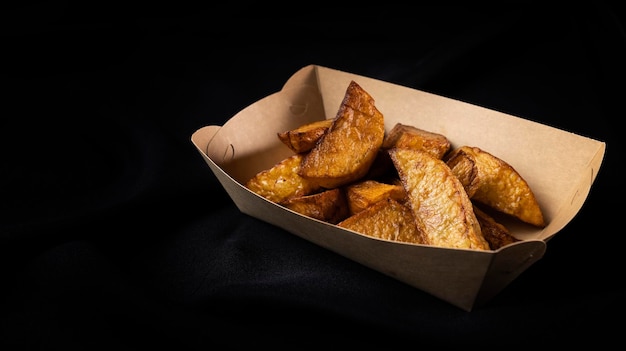 Baked potato slices in paper box rustic style fast food on black background