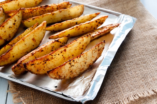 Запеченные картофельные дольки на подносе - домашний органический овощ, веганский дольки картофеля