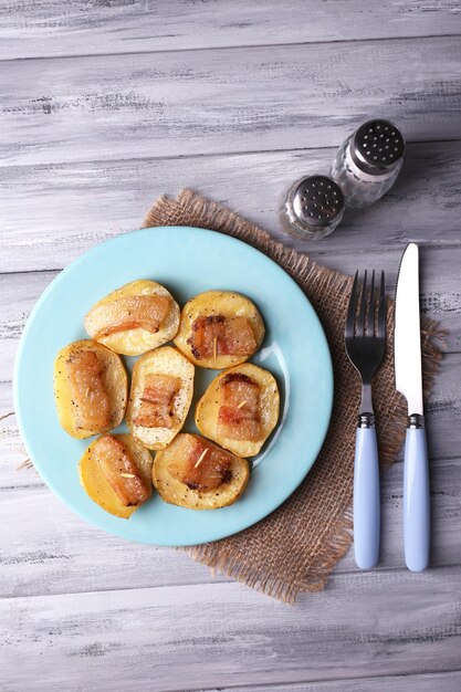 Foto patate al forno con pancetta sulla piastra su fondo di legno