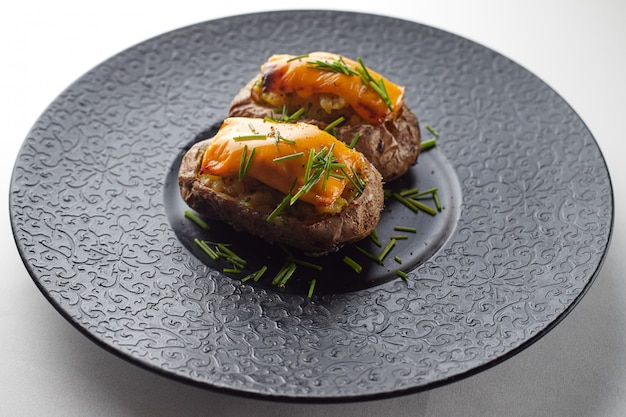 Baked potato with cheese and herbs on a black plate