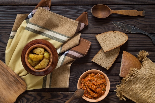 Baked potatoes in a clay pot bread and sauce on a wooden table