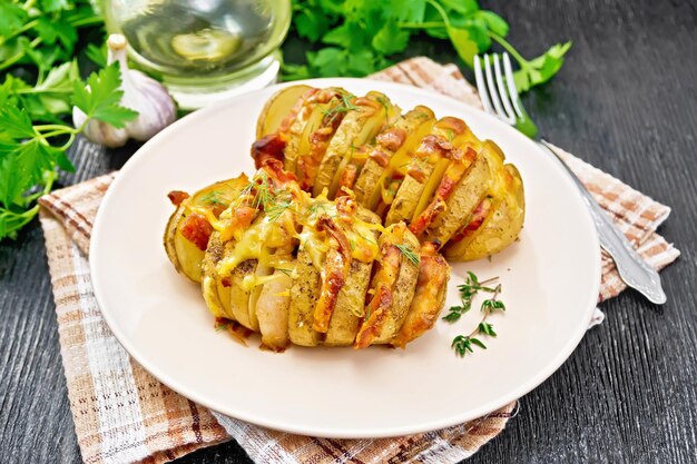 Baked potatoes layered with smoked bacon and cheese in a plate on a napkin against wooden board background