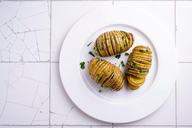 Baked potatoes on a white plate on white ceramic table.