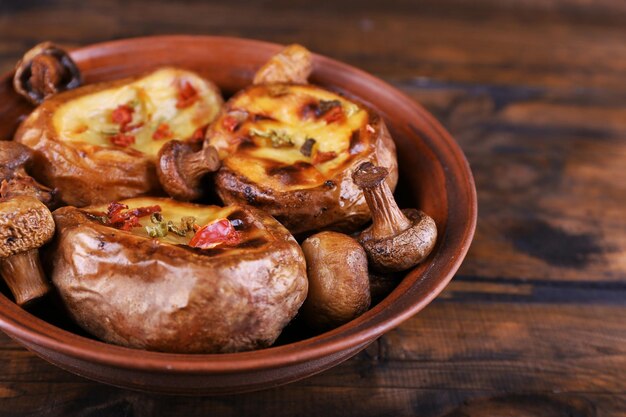 Baked potatoes with mushrooms in bowl on wooden background