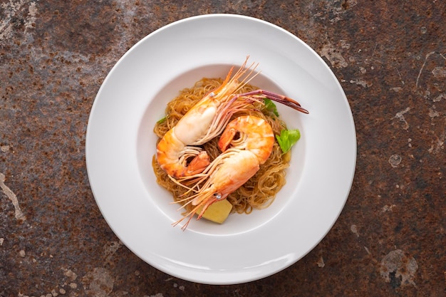 Baked prawns with vermicelli casseroled shrimps with glass noodles in white simply ceramic plate on rusty texture background top view flat lay river prawn