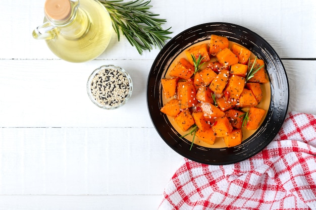 Baked pumpkin pieces with spices and herbs on white wooden background.