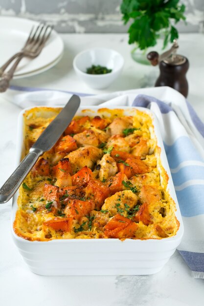 Baked pumpkin with chicken, spices and cream sauce in a white ceramic form on a light table. Selective focus.