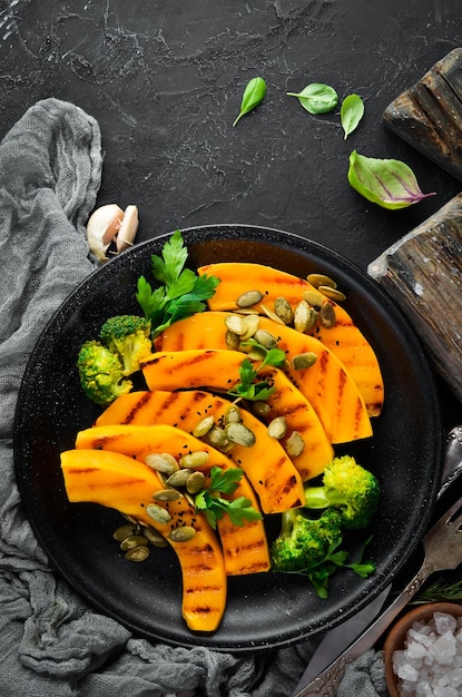 Baked pumpkin with pumpkin seeds and broccoli On a black background Top view Free space for your text