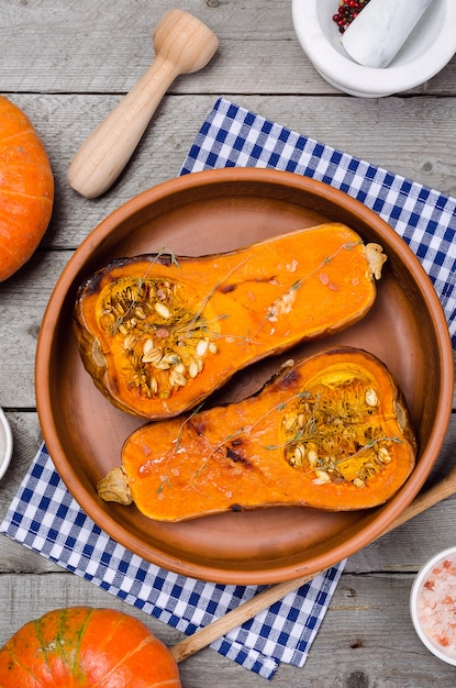 Baked pumpkin with thyme in a clay dish on a blue napkin, on a wooden table