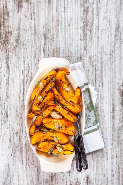 Baked pumpkin with thyme and seeds on a wooden background