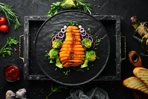 Baked pumpkin with vegetables on a black plate Top view Free copy space