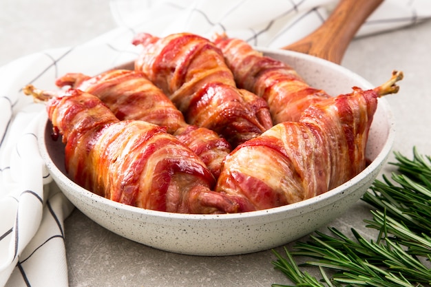 Baked quail wrapped in bacon in a frying pan with spices