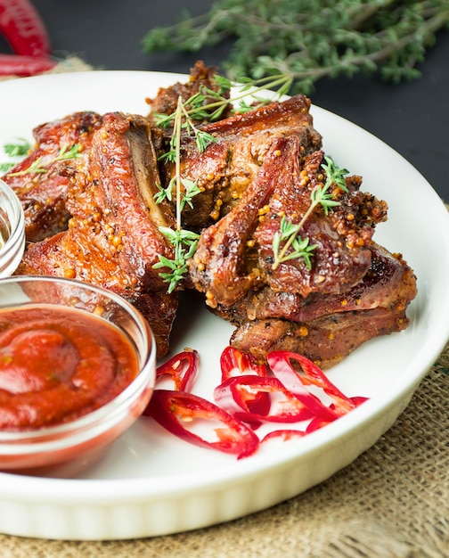 Baked ribs on a white dish Grilled ribs with spices and herbs on a dark background Food backgroundCloseup