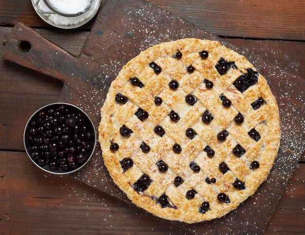 Baked round black currant pie on wooden table