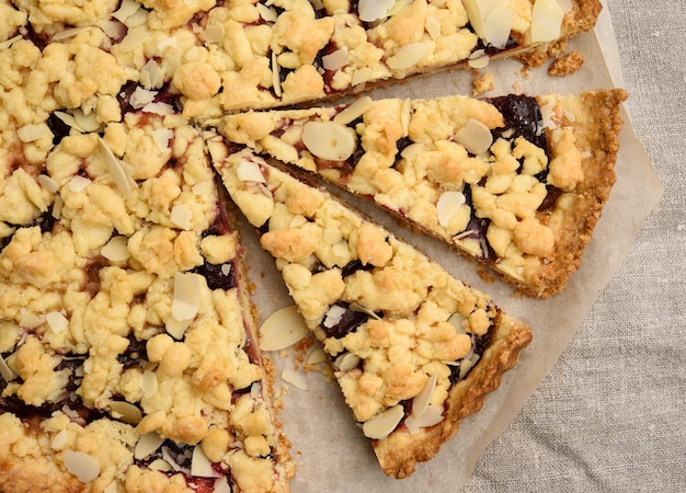 baked round crumble pie with plum cut into pieces on a black background top view