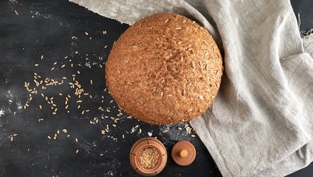 Baked round rye bread with sunflower seeds on a beige textile napkin, wooden background