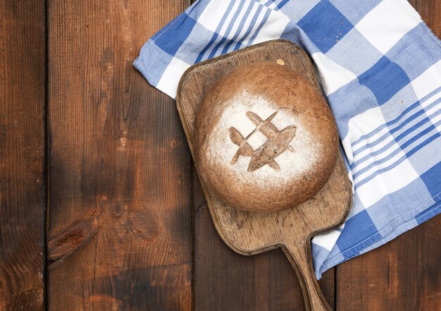 Baked round rye flour bread on brown wooden board, top view