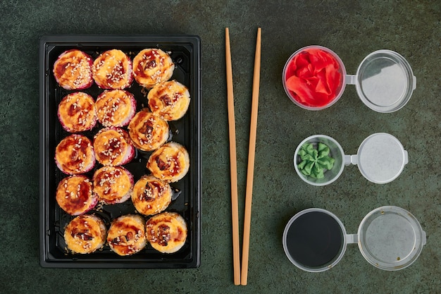 Baked salmon and eel rolls in a plastic takeout tray jars with ginger wasabi and soy sauce