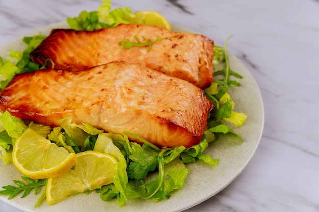 baked salmon fillet with green salad on gray plate.