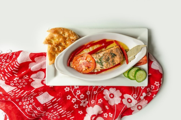 Baked salmon fillet with pita bread cucumber tomato in a dish isolated on colorful table cloth top view on grey background